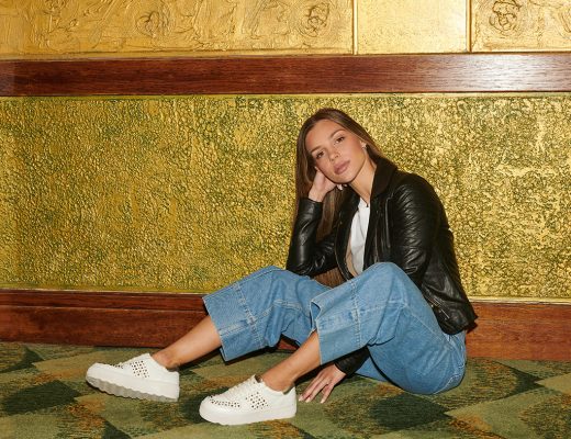 Woman poses wearing jeans, a leather jacket and metallic trainers