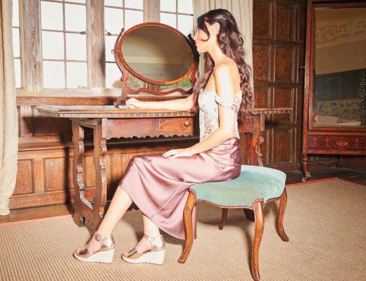A woman wearing wedge sandals, a corset and slip sits at her dressing table